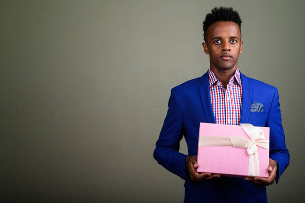 Young handsome African businessman holding gift box against colo - Foto, immagini