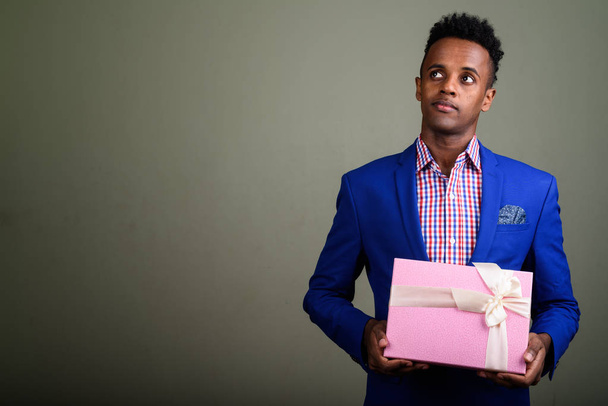 Young handsome African businessman holding gift box against colo - Foto, Bild