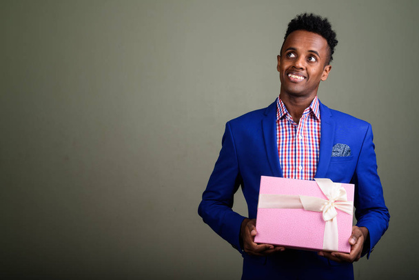 Young handsome African businessman holding gift box against colo - Photo, image