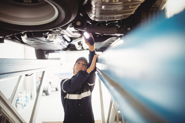 Nainen mekaanikko tutkii auton taskulamppu korjaus autotallissa
 - Valokuva, kuva