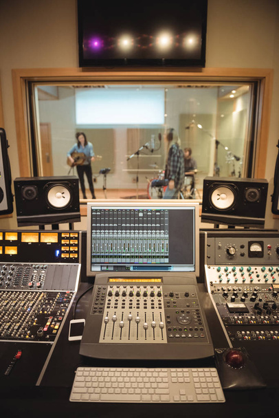 Звукорежиссер в студии звукозаписи с музыкантами на заднем плане
 - Фото, изображение