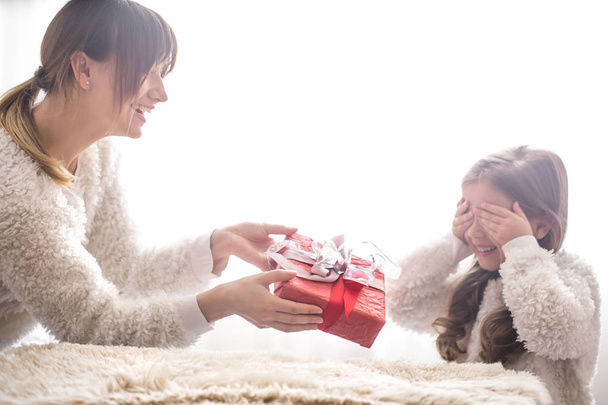 Karácsonyi és újévi koncepció, anya ad ajándékba egy kis aranyos lánya, egy hely a szöveg a világos háttér - Fotó, kép