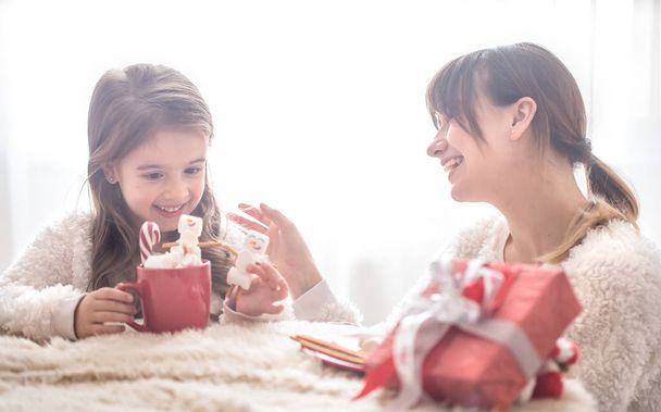 Anya és lánya aranyos eszik karácsonyi édesség a nappaliban, a világos háttér, a családi értékek és ünnepi hangulatot - Fotó, kép