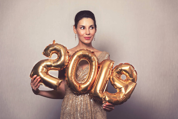 Happy New Year. Beautiful Woman with Balloons Celebrating new years Eve Party. Smiling Girl in Bright Shiny Dress with 2019 Gold Number Balloons Fun At Celebration - Foto, imagen