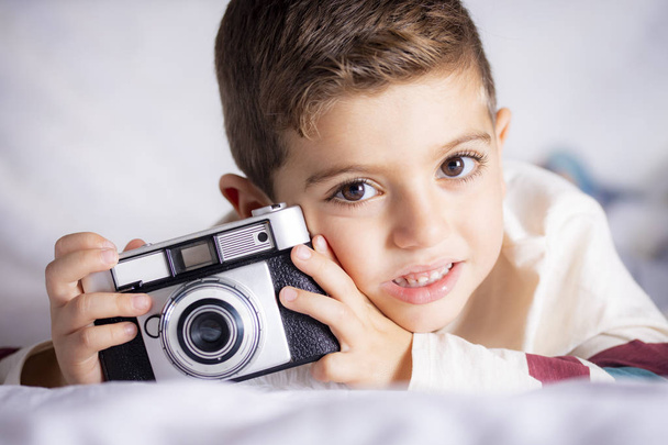 Mooie jongen met een fotograferen camera in het bed - Foto, afbeelding