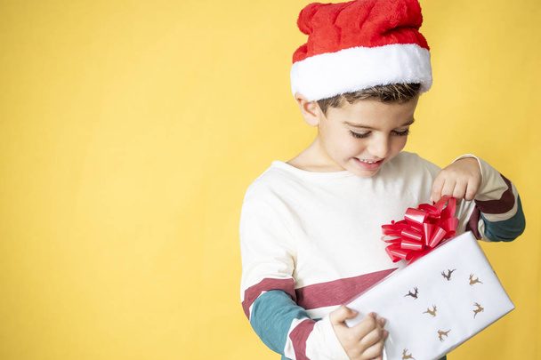 Niño pequeño con un regalo sobre un fondo amarillo el día de Navidad
 - Foto, Imagen