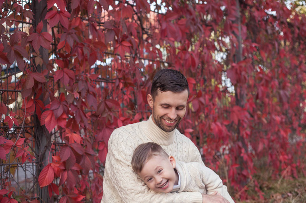 Dad and little son walk in the autumn park. Bright, warm autumn. Red leaves. Cozy. Portrait of dad and son in knitted sweaters. - Foto, immagini