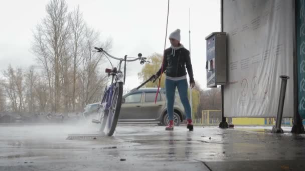 Młoda dziewczyna myje jej rower w myjni samochodowej - Materiał filmowy, wideo