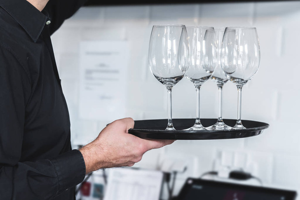Waiter carrying tray with empty glasses for red wine - Foto, imagen