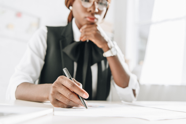selective focus of african american female adult architect in glasses using pen and working on documents in office - Photo, Image