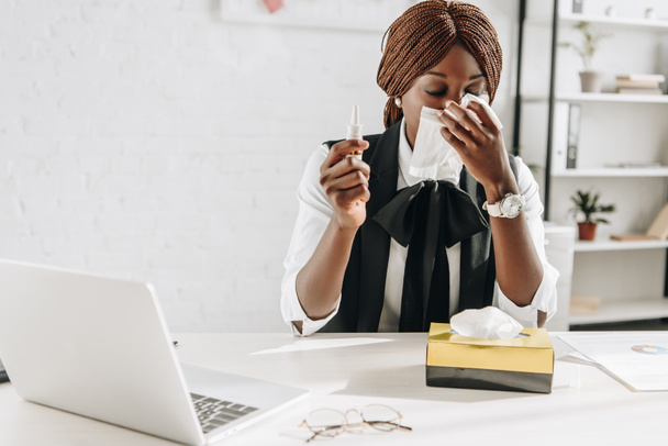 kranke afrikanisch-amerikanische erwachsene Geschäftsfrau, die an Erkältung leidet und Gewebe am Schreibtisch im Büro benutzt - Foto, Bild