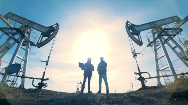 Два работника с подсветкой стоят между двумя нефтяными вышками
 - Кадры, видео