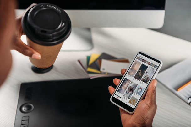cropped view of african american female businesswoman holding coffee to go and smartphone with pinterest app on screen - Foto, afbeelding