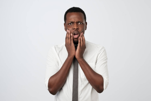 Δυστυχισμένος αφρικανική αρσενικό με δυσαρέσκεια έκφραση, συνοφρυώματα πρόσωπο, λαμβάνει κακές ειδήσεις. Απογοητευμένος νεαρός άνδρας στο λευκό πουκάμισο και γραβάτα - Φωτογραφία, εικόνα
