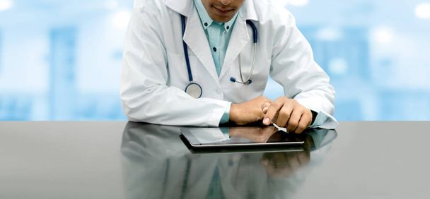 Médecin assis à table avec tablette dans le bureau de l'hôpital. Personnel médical et service médical
. - Photo, image