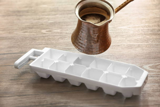 Pouring of coffee from jezve into ice tray on table - Photo, Image