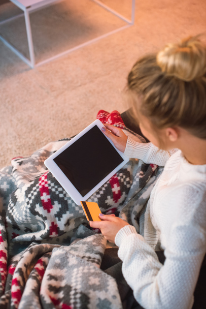 kredi kartı tutan ve online alışveriş için Noel zamanda dijital tablet kullanarak kanepede oturan kadın kırpılmış görünümünü  - Fotoğraf, Görsel