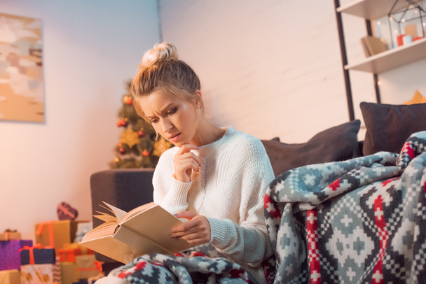 thughtful woman reading book at home on Christmas eve - Foto, afbeelding