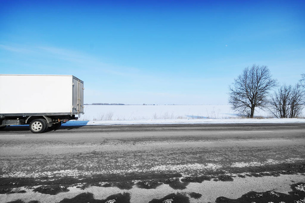 Weißer Kastenwagen auf winterlicher Landstraße mit Schnee gegen blauen Himmel - Foto, Bild