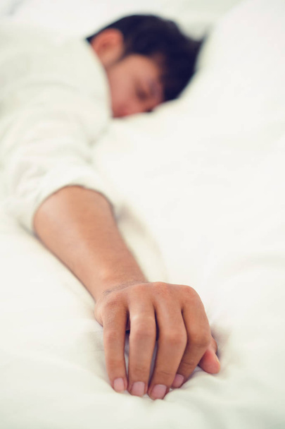 Jonge man slapen in wit linnen bed in de slaapkamer. - Foto, afbeelding