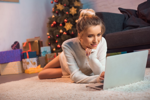 sonriente joven rubia acostada en el suelo usando el ordenador portátil en Navidad
 - Foto, imagen