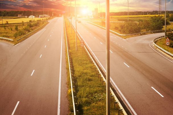 Venkovské cestě s automobily a les s poli proti světlé obloze s západ slunce - Fotografie, Obrázek