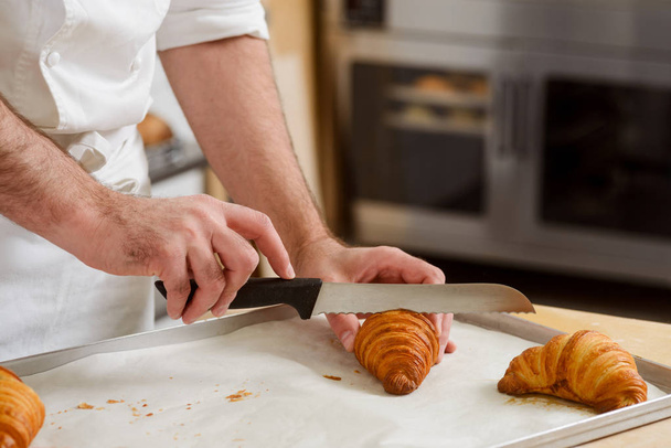 El hombre está cortando un croissant
 - Foto, Imagen