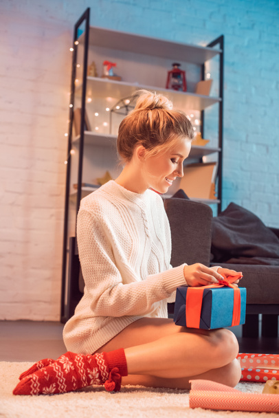 beautiful young blonde woman sitting and wrapping present at christmas time  - Фото, зображення
