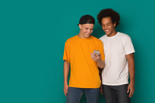 Two teenage guys using smatphone on blue background - Foto, Imagem