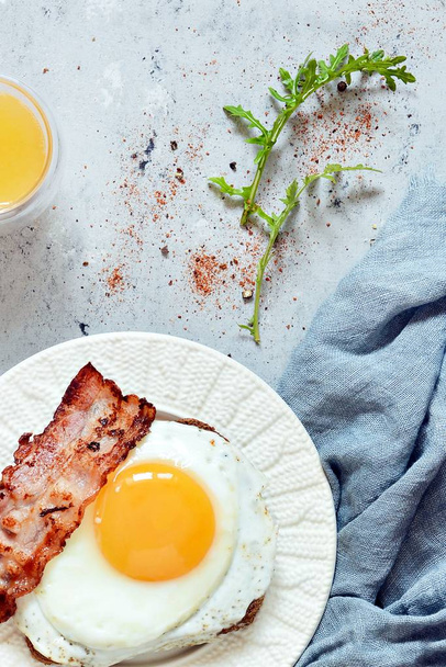 Deska se snídaní se sázenými vejci, slaninou a žitný chléb přípitek na šedém pozadí. Anglická snídaně, pomerančová šťáva - Fotografie, Obrázek