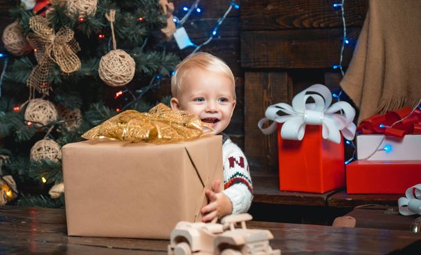New year presents in gift box for kids. Smiling funny child in Santa hat holding Christmas gift in hand. - 写真・画像