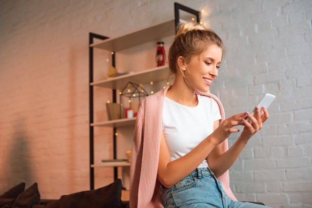smiling young blonde woman sitting and using smartphone at christmas time  - Fotó, kép