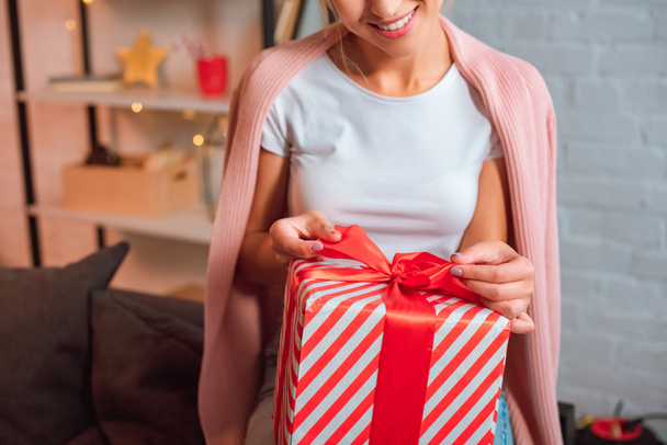 cropped view of smiling young woman tying bow on present at christmas time  - Фото, зображення