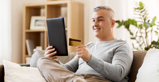 man with tablet pc and credit card on sofa at home - Фото, зображення