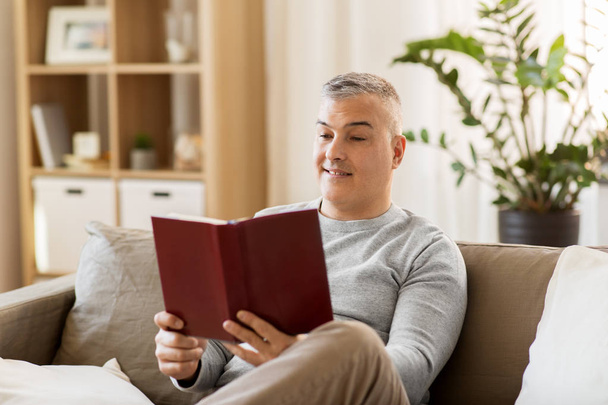 man sitting on sofa and reading book at home - Фото, зображення