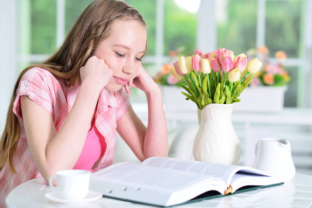 Cute schoolgirl sitting at table  and reading  at home - Foto, immagini