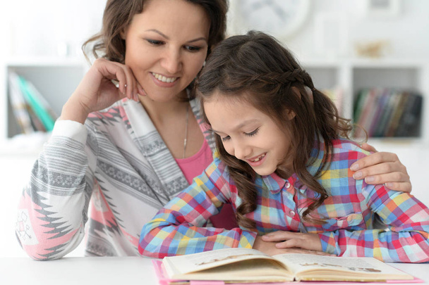 μικρό χαριτωμένο κορίτσι ανάγνωση βιβλίο με τη μητέρα στο τραπέζι στο σπίτι - Φωτογραφία, εικόνα