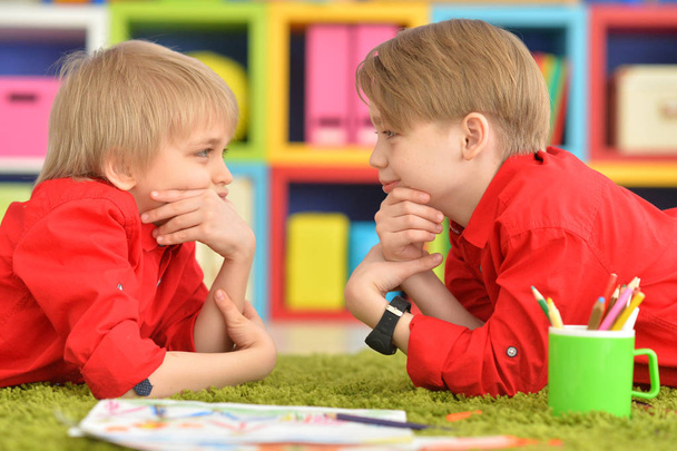 zwei lächelnde Jungen in roten Hemden, die auf dem Boden liegen und einander anschauen - Foto, Bild