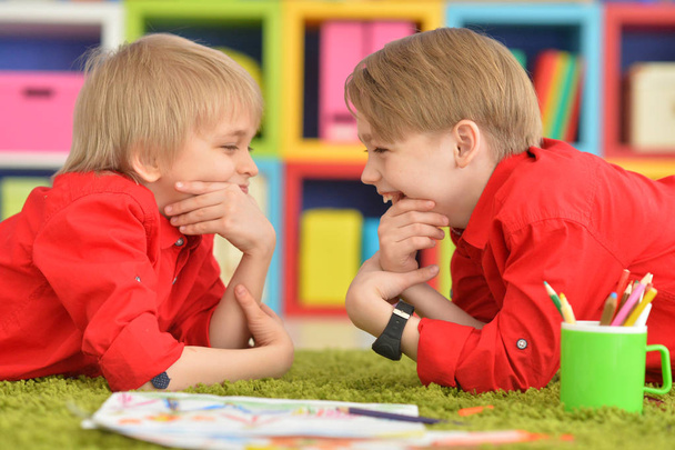 Two smiling boys in red shirts lying on floor and looking at each other - Foto, afbeelding