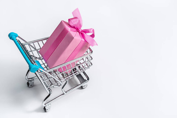 Gift box, in pink packaging, decorated with ribbons and bows in shopping cart. - Foto, imagen