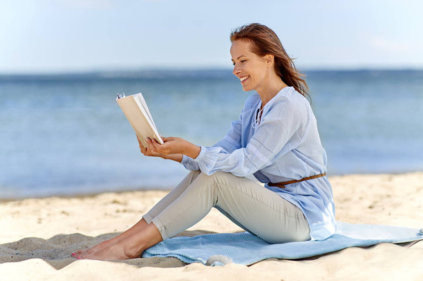 people and leisure concept - happy smiling woman reading book on summer beach - Foto, afbeelding