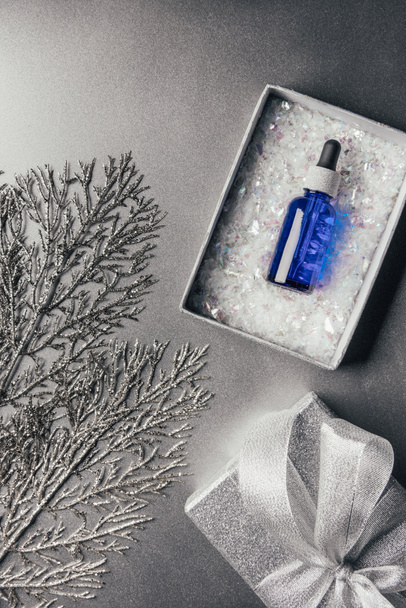 top view of christmas gift box with serum and decorated branches on silver - 写真・画像