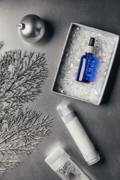 top view of serum in gift box, lotion, micellar water and christmas ball on silver  - 写真・画像
