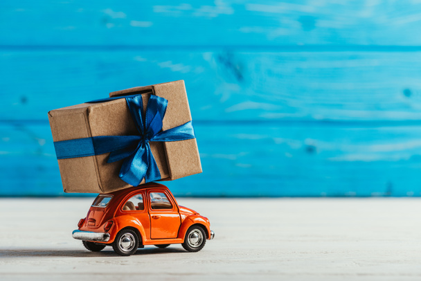 close-up shot of toy car with gift box on blue wooden background - Photo, Image