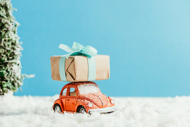 close-up shot of toy car with christmas gift box riding by snow made of cotton on blue background - Zdjęcie, obraz