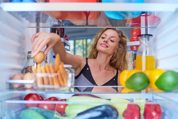 Bir kahvaltı yapmak için buzdolabı yumurtadan alarak Genç beyaz bir kadın. Buzdolabı içinde alınan resim. - Fotoğraf, Görsel