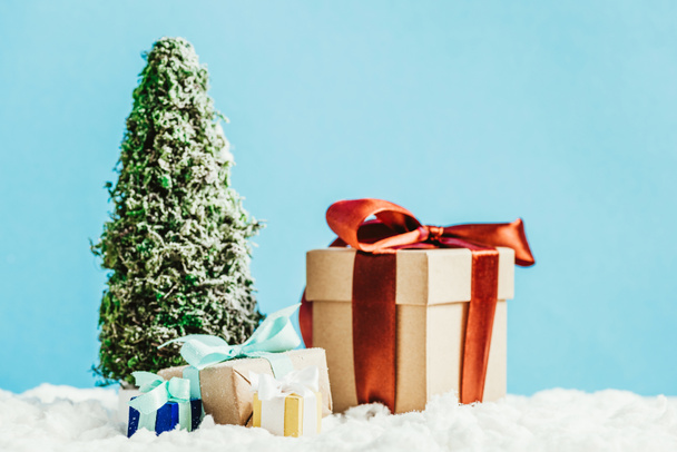 primer plano de regalos de Navidad y árbol de Navidad en miniatura de pie sobre la nieve sobre fondo azul
 - Foto, Imagen