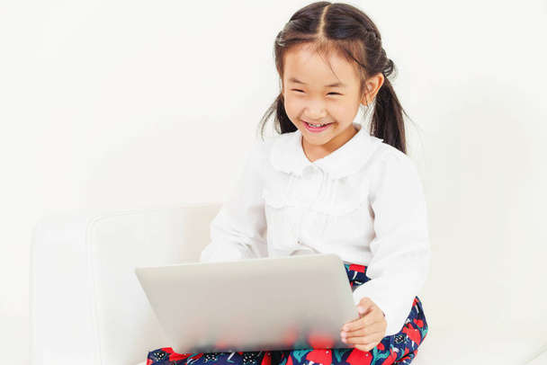 Klein gelukkig kind met behulp van laptopcomputer zittend op de witte Bank. Jeugd levensstijl. - Foto, afbeelding