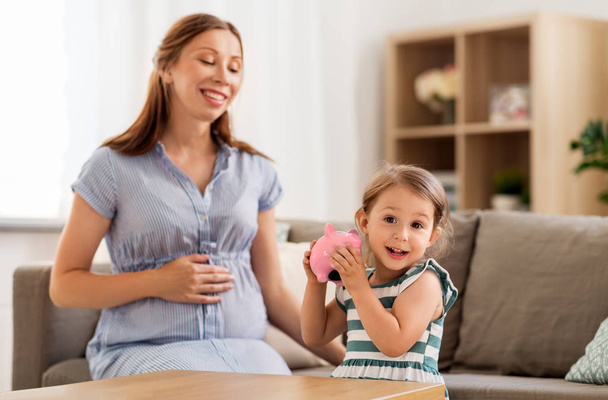 pregnant mother and daughter with piggy bank - Photo, Image