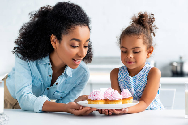 africano americano madre y hija buscando en casero cupcakes en cocina
 - Foto, Imagen